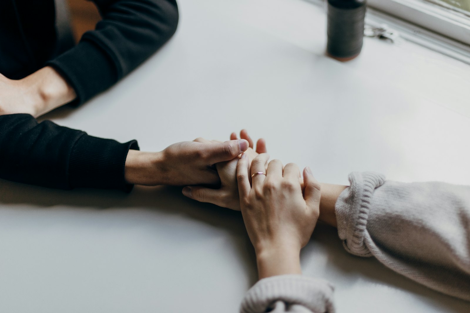One person gently holding another person's hands across a table in support